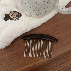 Detail of handmade acetate hair comb with 14 silver metal teeth on a wooden surface