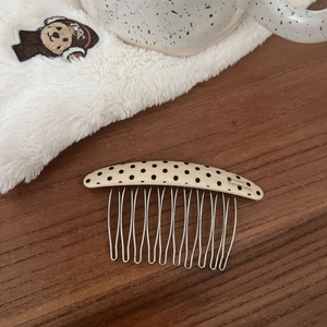 Macro detail of cream polka dot acetate hair comb with ten metal teeth on a wooden surface