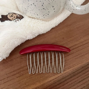 Detail of vintage burgundy acetate hair comb with 12 silver metal teeth on a wooden table