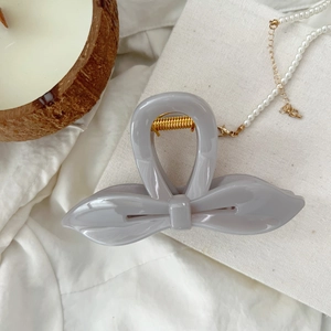 Détail de la pince à cheveux papillon grise avec ressort doré sur tissu texturé blanc