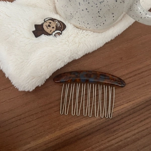 Detail of tortoiseshell acetate hair comb with silver metal teeth on a wooden surface