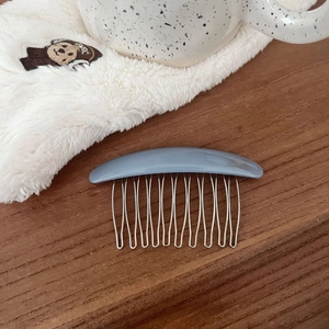 Close-up of a blue acetate hair comb with silver metal teeth on a wooden surface