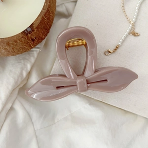 Détail d'une pince à cheveux papillon en résine rose poudré sur un fond en tissu esthétique