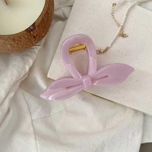 Pince à cheveux rose en forme de nœud avec ressort doré sur fond de tissu élégant
