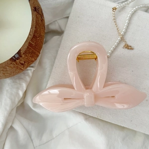 Détail d'une pince à cheveux nœud rose avec ressort doré sur un fond en tissu doux