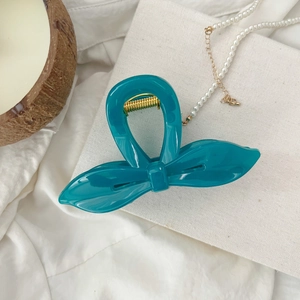 Détail de la pince à cheveux noeud bleu avec ressort en métal doré sur tissu blanc