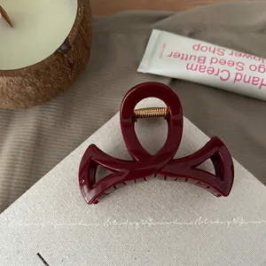 Détail de la pince à cheveux en résine bordeaux avec ressort doré sur tissu beige