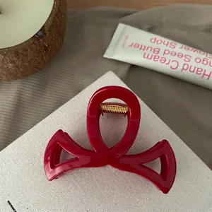 Détail d'une pince à cheveux rouge foncé brillante avec ressort doré et design croisé
