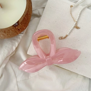 Pince à cheveux rose en forme de nœud avec ressort doré sur fond blanc esthétique