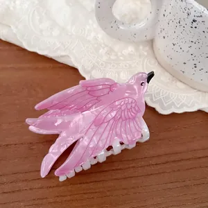 Detailed view of an elegant pink pearlescent bird-shaped hair claw on a wooden surface