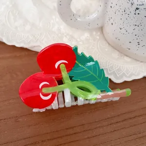 Detail view of a glossy red cherry hair claw clip with green leaves on a lace background
