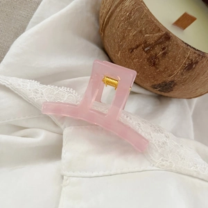 Detail shot of a translucent pink square hair claw clip with golden metal spring
