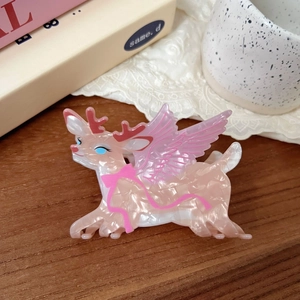 Detailed reindeer hair claw clip with pink wings and shimmery acetate finish on wood desk