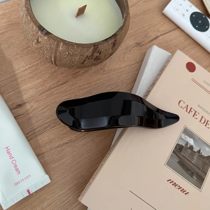 Glossy black wave-shaped hair claw clip on wooden table with cozy lifestyle decor