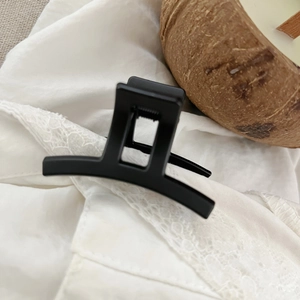 Detail of matte black square hair claw clip with metal spring on white lace fabric