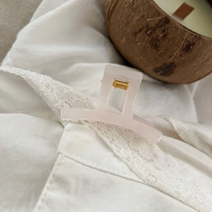 Close-up of translucent pale pink square hair claw clip with golden spring on lace fabric