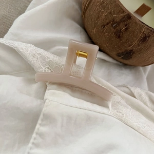 Detail of pink rectangular hair claw clip with golden spring on white lace fabric