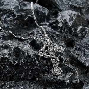 Macro detail of gothic silver cross necklace with skull and dragon on dark stone