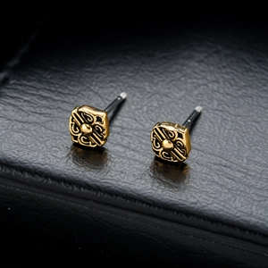 Macro detail of vintage gold hollowed-out stud earrings on black leather display