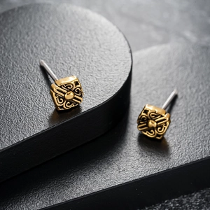 Macro shot of gold square stud earrings with vintage hollowed patterns on a black stand