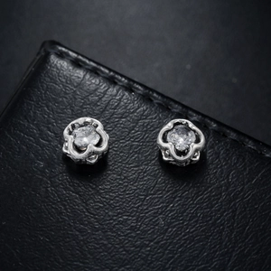 Silver flower magnetic ear clips with round zircon center on black leather background