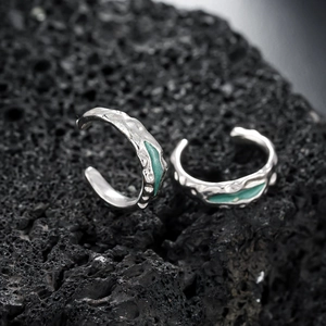 Macro shot of silver lava textured ear cuffs with mint green enamel on volcanic rock
