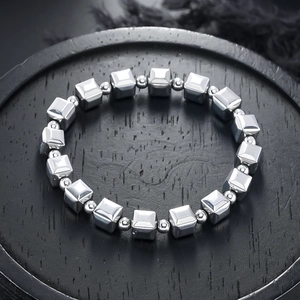 Geometric silver metallic bracelet with square beads on a black wooden tray