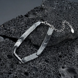 Close-up of arrow-shaped stainless steel chain links on a black volcanic rock surface