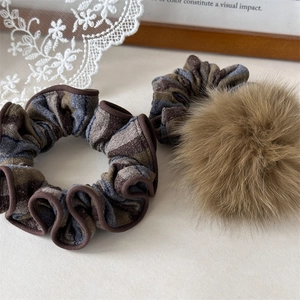 Dettaglio di elastico per capelli in maglia a righe e pompon marrone di peluche morbido