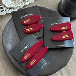 Three-piece set of deep red acetate hair clips with gold lettering on a chic display tray