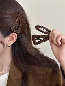 Detail of plush leopard print hair clip and gold hoop earring worn by a model