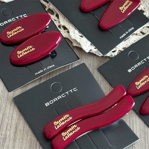 Detailed view of red acetate hair clips with gold logo on elegant lace background