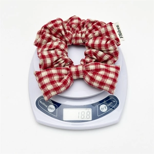 Close-up of a red and white gingham bow hair scrunchie showing fabric weight on a scale