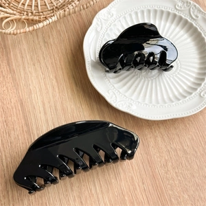 Détail de grandes pinces à cheveux noires brillantes sur un plateau en céramique blanc