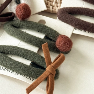 Détail de barrettes en feutre avec pompons orange et nœuds marron sur carte