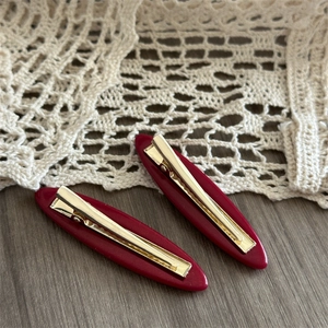 Set of two burgundy acetate bow hair clips with golden metal duckbill clips on wood