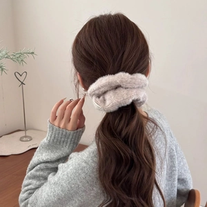Détail d'un chouchou en peluche crème porté sur les cheveux montrant la texture tricot