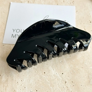 Détail d'une grande pince à cheveux noire brillante sur fond de marbre pour cheveux épais