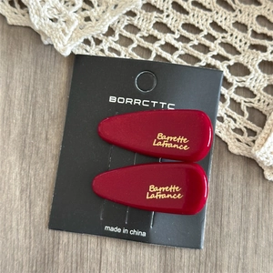 Close-up of two red acetate bow hair clips on display card over lace background