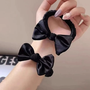 Detail showing a black satin bow hair tie with silky texture on a wrist and hand