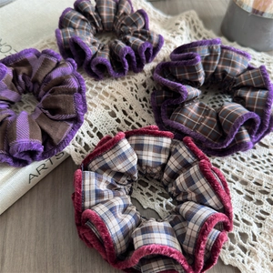 Detail of four plaid hair scrunchies with fuzzy edges on lace decor and art book background