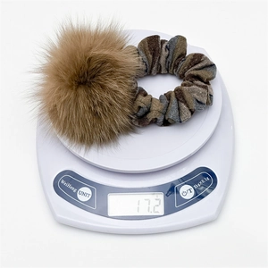 Dettaglio di un elastico per capelli a righe marroni con pompon su bilancia del peso di 17,2 g