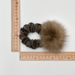Elastico per capelli in maglia a righe con pompon marrone mostrato su sfondo bianco