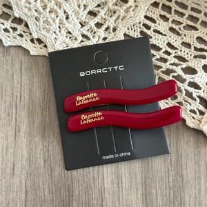 Detail of red wavy hair clips with gold lettering on elegant lace and wood background