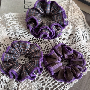 Close-up of three checkered fabric scrunchies with purple ruffled edges on white lace