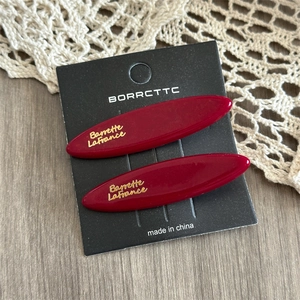 Close-up of deep red acetate hair clips with gold lettering on a black display card
