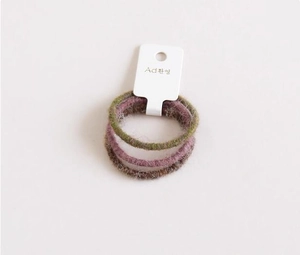 Vista dettagliata di tre elastici per capelli in velluto verde oliva, rosa e viola scuro