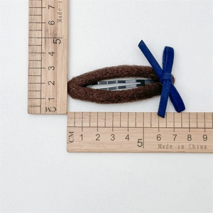 Détail d'une pince à cheveux en peluche marron avec un nœud bleu de 6 cm environ