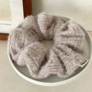 Gros plan d'un chouchou en tricot beige doux avec une texture pelucheuse sur un plateau blanc