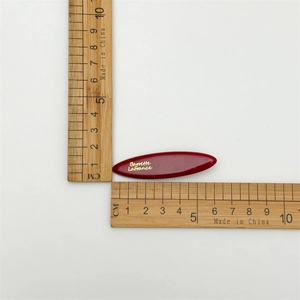 Macro shot of dark red acetate hair clip with gold lettering and dimension ruler